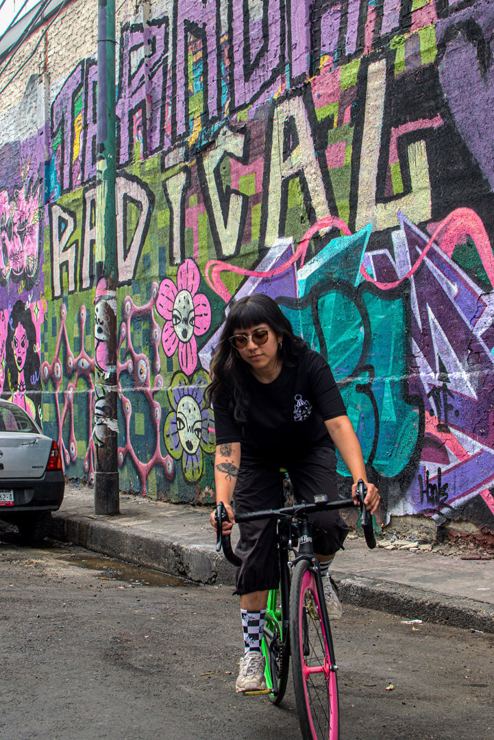 Ave Catmin con una bicicleta frente a un mural
